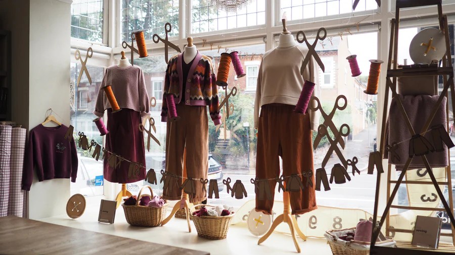 Fall window display at Guthrie & Ghani showcasing handmade clothes on models and decorative sewing-themed garlands